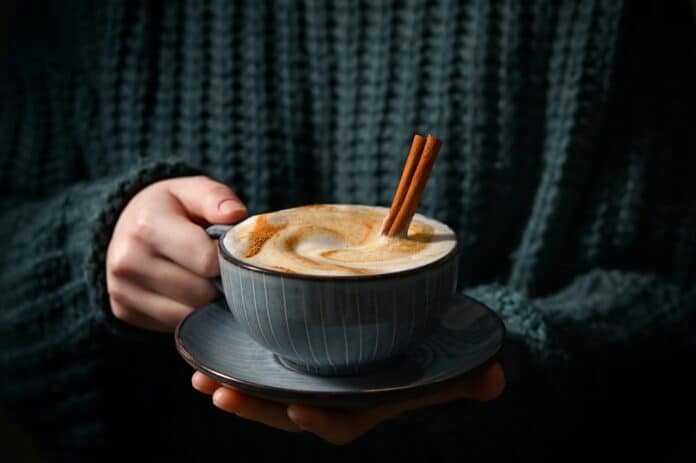 Woman,Holding,Cup,Of,Cappuccino,With,Cinnamon,Sticks