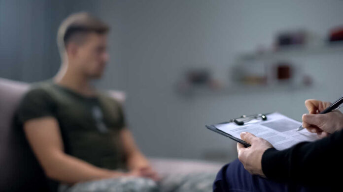 Psychologist,Making,Notes,During,Therapy,Session,With,Sad,Male,Soldier,