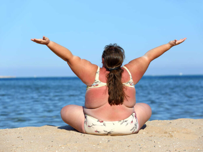 Overweight,Woman,Sitting,On,Beach,With,Hands,Up