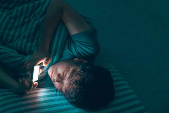 Sleepy,Tired,Teenage,Man,Under,The,Blanket,Using,Smartphone,With