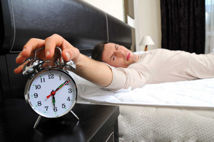 A,Man,Is,Sleeping,With,An,Alarm,Clock,In,Front