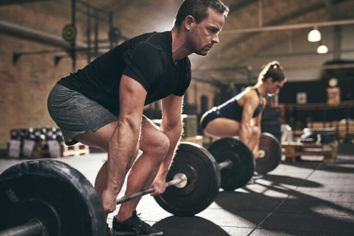 Sporty,Man,And,Woman,Are,About,To,Lift,Barbells,In