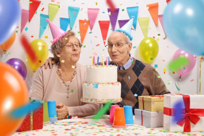 Senior,Couple,Blowing,Candles,On,A,Birthday,Cake