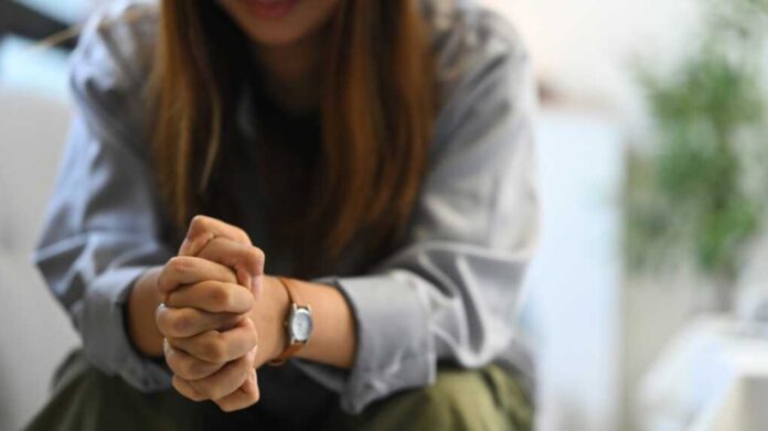 Depressed,Sad,Woman,Sitting,Alone,On,Sofa,With,Hands,Clasped.
