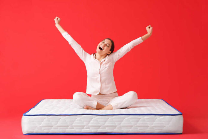 Happy,Young,Woman,Sitting,On,Mattress,Against,Color,Background