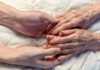A younger persons hand gently holding an elderly persons hand on a quilted surface