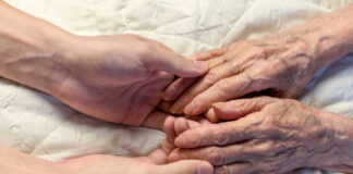 A younger persons hand gently holding an elderly persons hand on a quilted surface