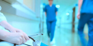 A healthcare professional holding a stethoscope in a hospital corridor