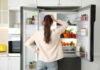 Morning Habit Silently Breaking Your Bones A woman standing in front of an open refrigerator filled with various fruits and vegetables