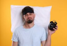 Is Your 3 A.M. Wake-Up Normal? Man wearing a sleep mask holding an alarm clock with a frustrated expression