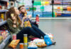 Ultra-Processed Foods Meet Tobacco Addiction Criteria A young couple sitting on the floor of a grocery store enjoying snacks