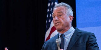 A man speaking into a microphone at a podium with an American flag in the background