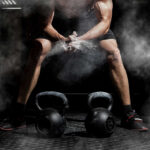 Athlete preparing to lift kettlebells in a gym with chalk dust in the air