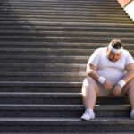 An exhausted man in sportswear sitting on outdoor stairs, looking down.