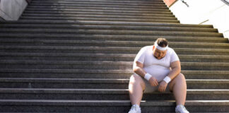 An exhausted man in sportswear sitting on outdoor stairs, looking down.