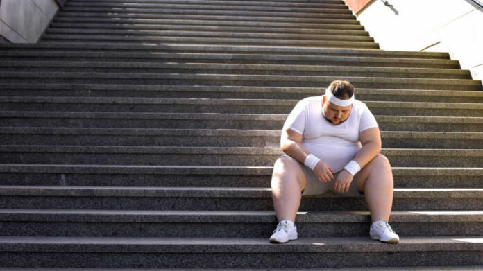 An exhausted man in sportswear sitting on outdoor stairs, looking down.