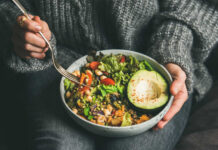A person holding a bowl of colorful salad with avocado and greens