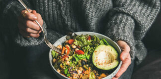 A person holding a bowl of colorful salad with avocado and greens