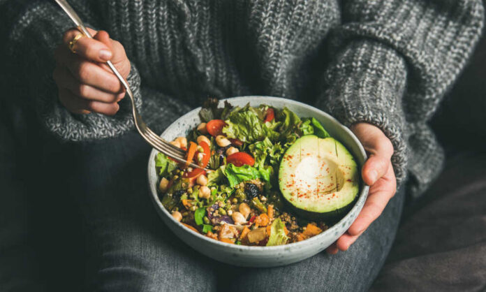 A person holding a bowl of colorful salad with avocado and greens