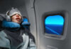 A passenger sleeping on an airplane with headphones and an eye mask