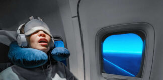 A passenger sleeping on an airplane with headphones and an eye mask