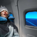 A passenger sleeping on an airplane with headphones and an eye mask
