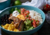 A vibrant bowl filled with grilled chicken, rice, black beans, corn, guacamole, and fresh vegetables