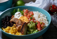 A vibrant bowl filled with grilled chicken, rice, black beans, corn, guacamole, and fresh vegetables