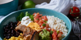 A vibrant bowl filled with grilled chicken, rice, black beans, corn, guacamole, and fresh vegetables