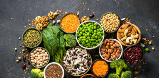 An assortment of legumes, nuts, and fresh vegetables arranged in bowls on a dark surface