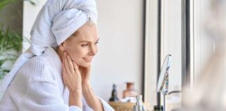 Woman in a bathrobe with a towel on her head, smiling at her reflection in a mirror