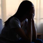 A silhouette of a person sitting with their head in their hands, conveying distress