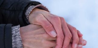 Two hands clasped together, one wearing a black jacket