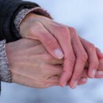 Two hands clasped together, one wearing a black jacket