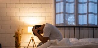 A person sitting on a bed with their head in their hands, expressing distress