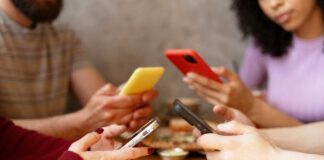 Group of friends sitting at a table, each using their smartphones