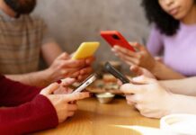 Group of friends sitting at a table, each using their smartphones