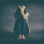 A person sitting on the floor with their arms wrapped around their knees, conveying a sense of distress