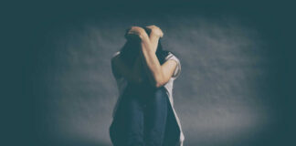 A person sitting on the floor with their arms wrapped around their knees, conveying a sense of distress