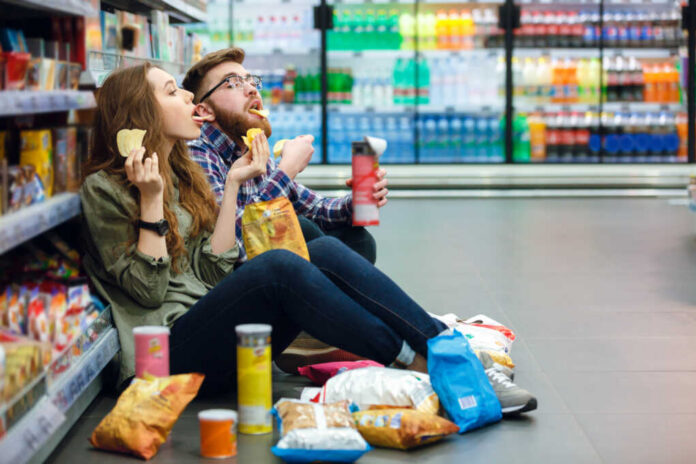 A young couple sitting on the floor of a grocery store enjoying snacks