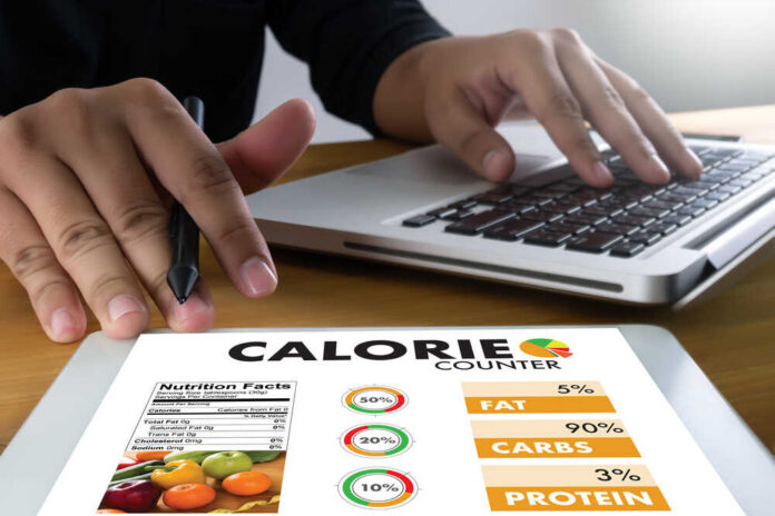 shutterstock_757192321.jpg Person using a calorie counter app on a tablet while working on a laptop