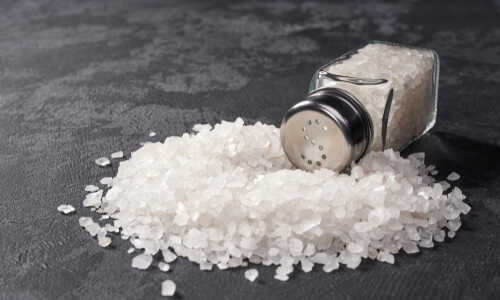 shutterstock_1334954570.jpg A glass salt shaker tipped over with salt spilling out