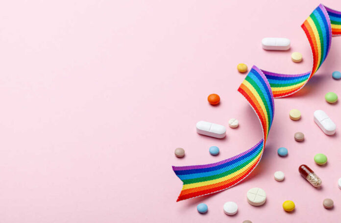 Colorful pills and a rainbow ribbon on a pink background