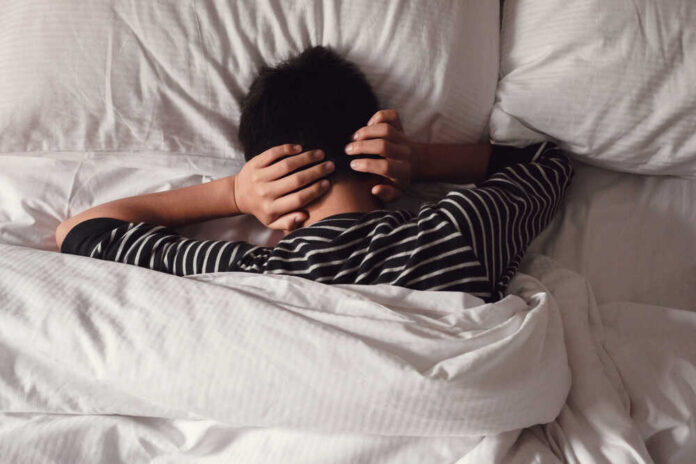 shutterstock_1649044030.jpg Child lying in bed with hands over ears