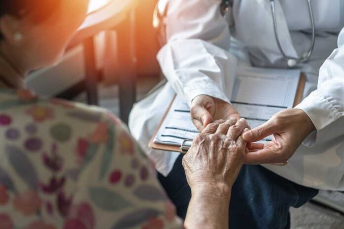A doctor holding the hand of an elderly patient during a consultation