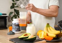 Person preparing a protein shake with fruits and whey protein powder in a kitchen