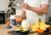 Person preparing a protein shake with fruits and whey protein powder in a kitchen