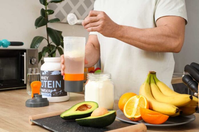 Person preparing a protein shake with fruits and whey protein powder in a kitchen