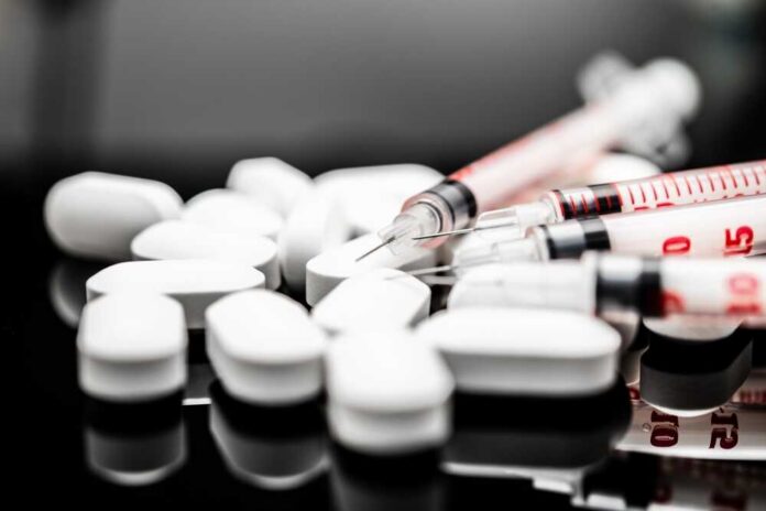White pills and syringes arranged on a reflective surface