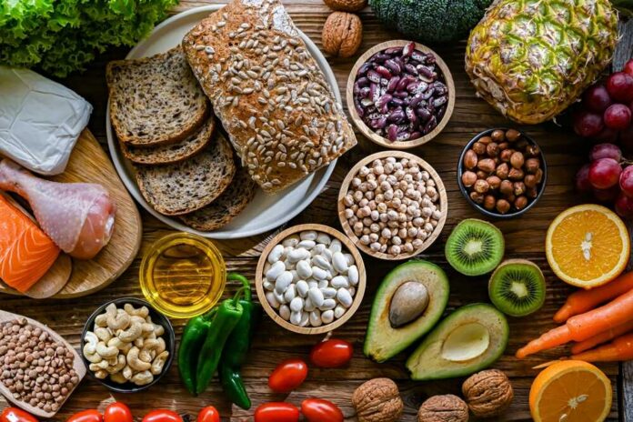 shutterstock_2483555019.jpg A variety of fresh foods including vegetables, fruits, grains, and proteins arranged on a wooden surface